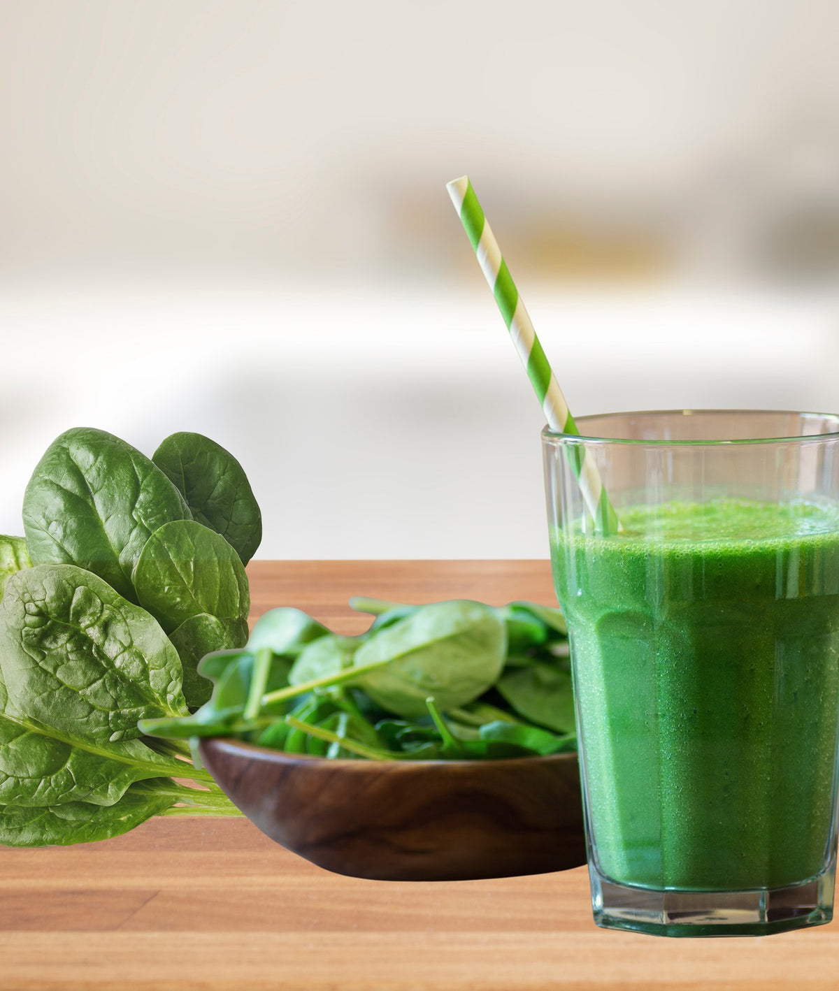 Fresh spinach leaves in a wooden bowl beside a green spinach smoothie.