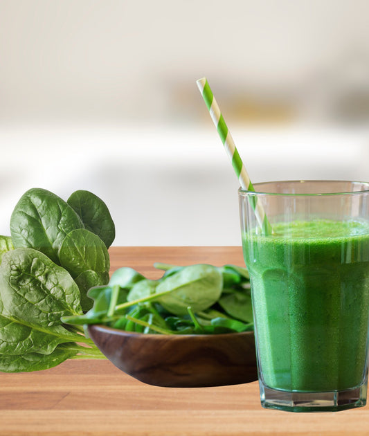 Fresh spinach leaves in a wooden bowl beside a green spinach smoothie.